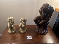 Two small soapstone The Thinker bookends and one larger dark brown ceramic The Thinker statue on a table.