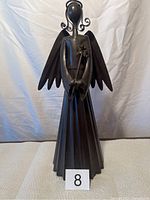 Front view of large black metal tin angel figurine with wings, holding a star, standing on flat surface against a white backdrop.