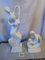 Front view of two white abstract sculptures: tall man and woman figure and shorter woman and child figure.