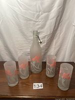 Photo of the set including the frosted glass decanter with stopper and four frosted water glasses, all with orange flower and white stems etched design.