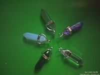 Five crystal point pendants arranged on a green background showing different colors and material types with silver caps and loops.