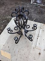 Top and angled side view of large black metal chandelier showing six curved arms and central connecting rod with curled decorative metalwork.