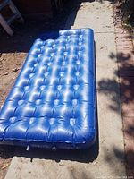 Blue inflatable air mattress placed on the ground outdoors, showing full length and tufted air chambers.