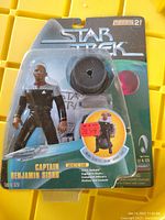 Front view of sealed Captain Benjamin Sisko action figure in blister packaging showing figure, chair, and accessories.