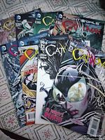 Photo showing a stack of Catwoman New 52 comic books, featuring covers visible with Catwoman on front in dynamic poses, papers on patterned cloth background.