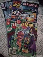 Photo showing a mixed lot of 9 comic books including GI Combat Haunted Tank series, Supreme #1, Brigade #3, Marvel Age #127, The New Teen Titans #23 and #25, and The Outsiders.