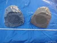Pair of large outdoor rock speakers placed on blue tarp with measuring scales for size reference.