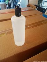 Photo of a small clear plastic hand sanitizer bottle with black flip-top cap standing on a large cardboard case box.