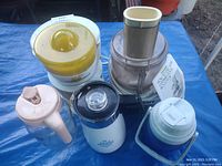 Photo of the lot showing The Lemonader lemonade maker, Cuisinart food processor, coffee maker, thermos, and juice pitcher on a blue surface outdoors.