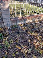 Metal bike rack placed outdoors near a fence surrounded by fallen leaves, showing the full length and individual slots for holding bikes.