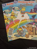 Photo showing two copies of 'Rainbow Brite and the Star Stealer' official movie adaptation comics by DC Comics, featuring colorful illustrated covers with Rainbow Brite on a rainbow and various characters.