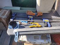 Top view of table with assorted tools including clamps, pipe cutter, extension cord, ruler, and wastebasket.