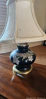 Black ceramic base lamp with hand-painted floral design and worn beige fabric square shade