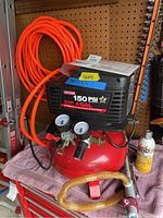 Craftsman air compressor with attached pressure gauges and regulator, orange air hose coiled on wall-mounted reel, yellow air hose with pneumatic tool attached, sitting on cabinet.