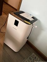 Front-left perspective of air purifier showing overall unit, power cord and manual on top