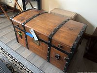 Closed view of the antique wooden trunk showing metal reinforcement bands and central latch.