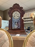 Full view of antique wooden Ansonia mantel clock with decorative carved detailing and visible pendulum inside glass panel.