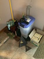 Wide view of lot showing broom, battery-powered flashlight, large plastic container with bird seed, bird feeder and boxes of suet cakes.