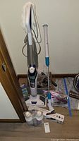 Full view of Bissell PowerFresh Deluxe steam mop vacuum standing upright with attached power cord and mop head. Nearby are grout cleaning accessories and liquid containers visible on floor.