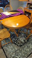 View of oak table top with inserted leaf, chairs around, purple cloth and items on table