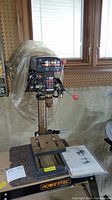 Front view of Craftsman bench top drill press with adjustable table and manual on table.