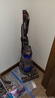 Full view of Dyson DC25 vacuum cleaner standing upright, showing handle, hose, canister, and cleaner head on floor mat.