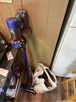 Full view of Dyson V8 Animalpro cordless vacuum on wall mount with wand and plastic bag of attachments on floor