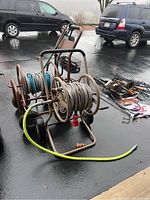 Wide view of two metal hose reels with attached hoses on wet pavement with vehicles in the background