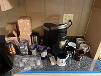Overall view of Keurig coffee maker with mugs, cups, and coffee filters on countertop