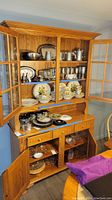 Frontal view of entire oak hutch with upper glass doors open, displaying shelves with dishes and lower cabinet doors open revealing storage area