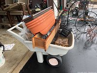 White Rubbermaid garden cart loaded with plastic planters, wooden window box planter, metal planter holders with coir liners shown inside the cart.