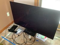 Front view of Samsung TV with cables, remote and stand on tiled floor