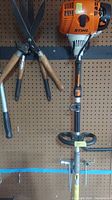 Stihl engine head and first set of wooden-handled attachments on pegboard