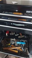Top drawer open showing various tools including hammers, ice scraper, paintbrushes, and small metal tools inside a black Craftsman toolbox.