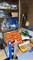 Shelf with various tools and hardware, orange plastic drawers, power cords, and hand tools