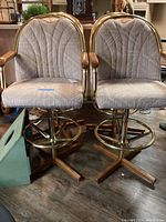 Four vintage swivel bar stools with brass bases and wooden armrests, upholstered in beige patterned fabric, arranged together indoors on wood floor.