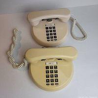 Top view of two vintage rotary-style telephones, showing push-button keypads and handsets, coiled cords on left.
