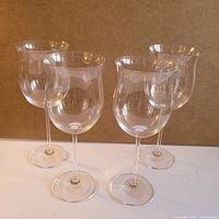 Four clear oversized Waterford Marquis lead-free crystal burgundy glasses with tall stems and rounded bowls, standing together on a flat surface, viewed frontally.