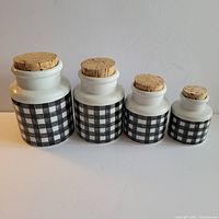 Front row side profile showing four graduated size black and white gingham patterned stoneware canisters with cork stoppers arranged by descending size.