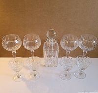 Full set of 9 crystal glassware items shown: 4 wine glasses, 4 cocktail glasses, and 1 decanter with stopper, all with detailed cross and olive cut designs.