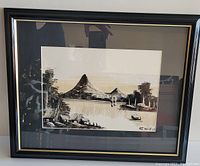 Framed black and white watercolor painting of Asian fishing village with mountains, water, boat, trees and village buildings. Signed by artist at bottom right.