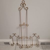 Three brass decorative plate holder racks shown together against a wall and floor including two smaller 14 inch racks and a taller 39 inch rack