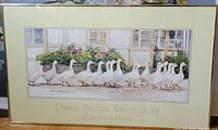 Front view of framed artwork titled 'Dinner Call' with watercolor depiction of a row of white ducks, floral garden and window background.
