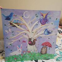 Canvas print titled 'Woodlot Wonderland' showing whimsical woodland animals and nature scene in pastel colors with a white tree and various animals including birds, squirrel, rabbit, and hedgehog.