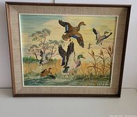 Framed oil painting showing multiple mallard ducks flying and landing on water with natural background, signed Rudy Schnabel.