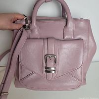 Front view showing top handles, front flap pocket with silver buckle, and adjustable strap laid over the handbag