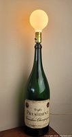 Full view of the green champagne bottle lamp lit with a round bulb on top.