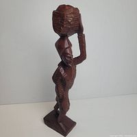 Front side view of the hand carved wooden African statue holding a basket on the head