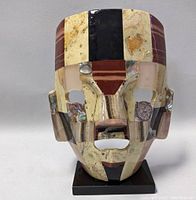 Front view of the Mayan Aztec mask showing mosaic semi-precious stones and facial features on a black base.
