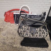 Five purses displayed on counter, including coral red, black and white color-blocked, houndstooth pattern, Tommy Hilfiger patterned, and black beaded clutch.